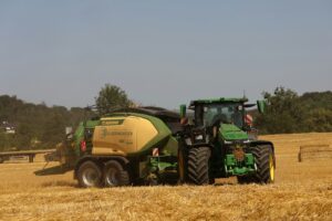 A green tractor bales hay in a golden field